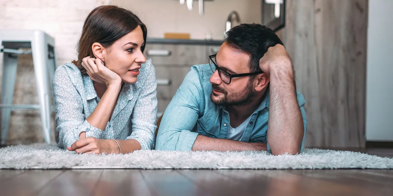 A couple laying on a rug engaging in conversation