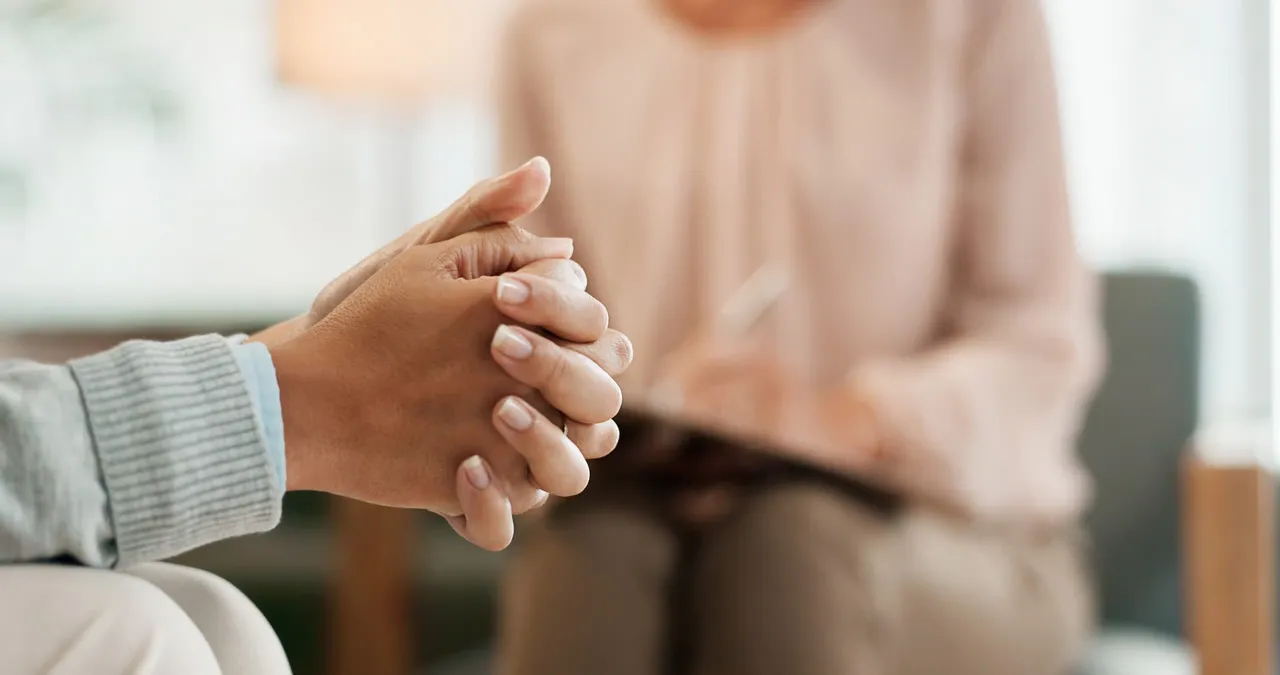 A person with their hands folder, with a therapist blurred in the background